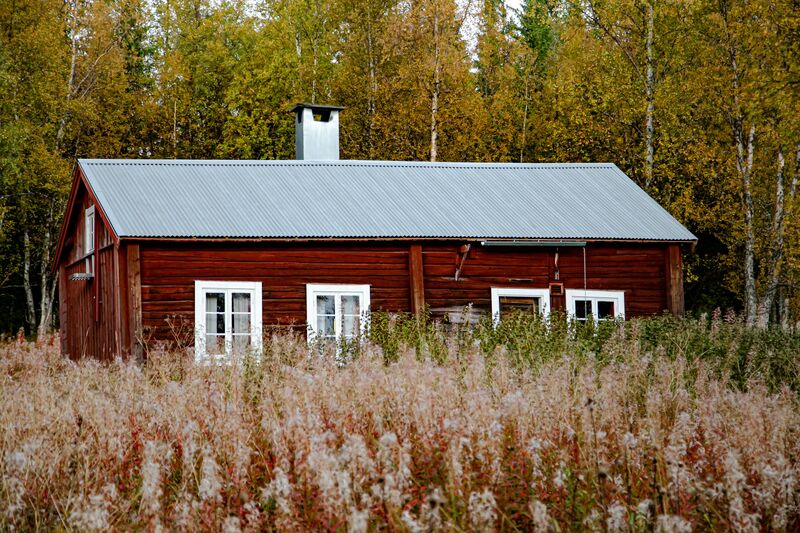 Punainen puutalo peltiaukolla.